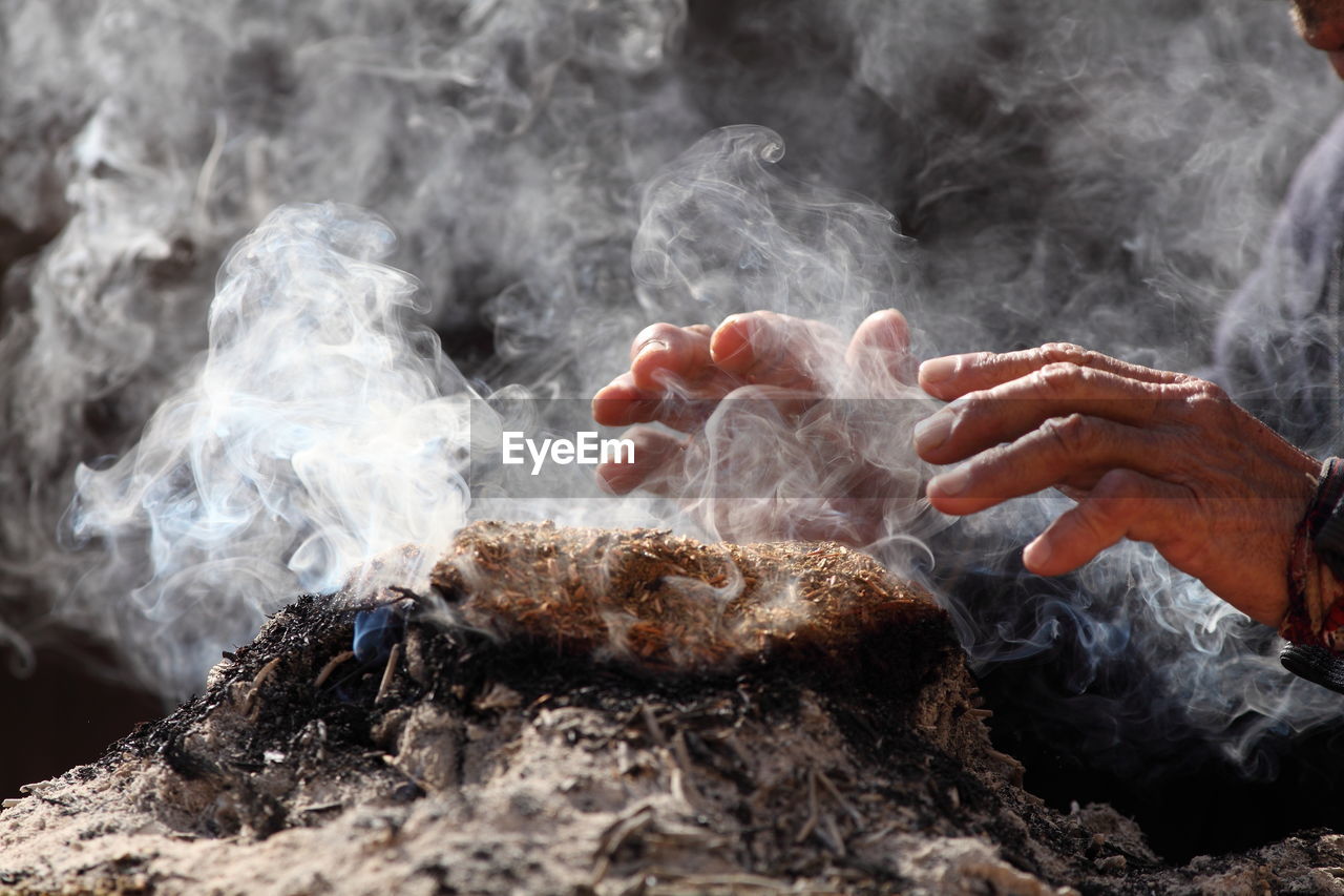 Cropped image of hand over smoke emitting from incense at temple