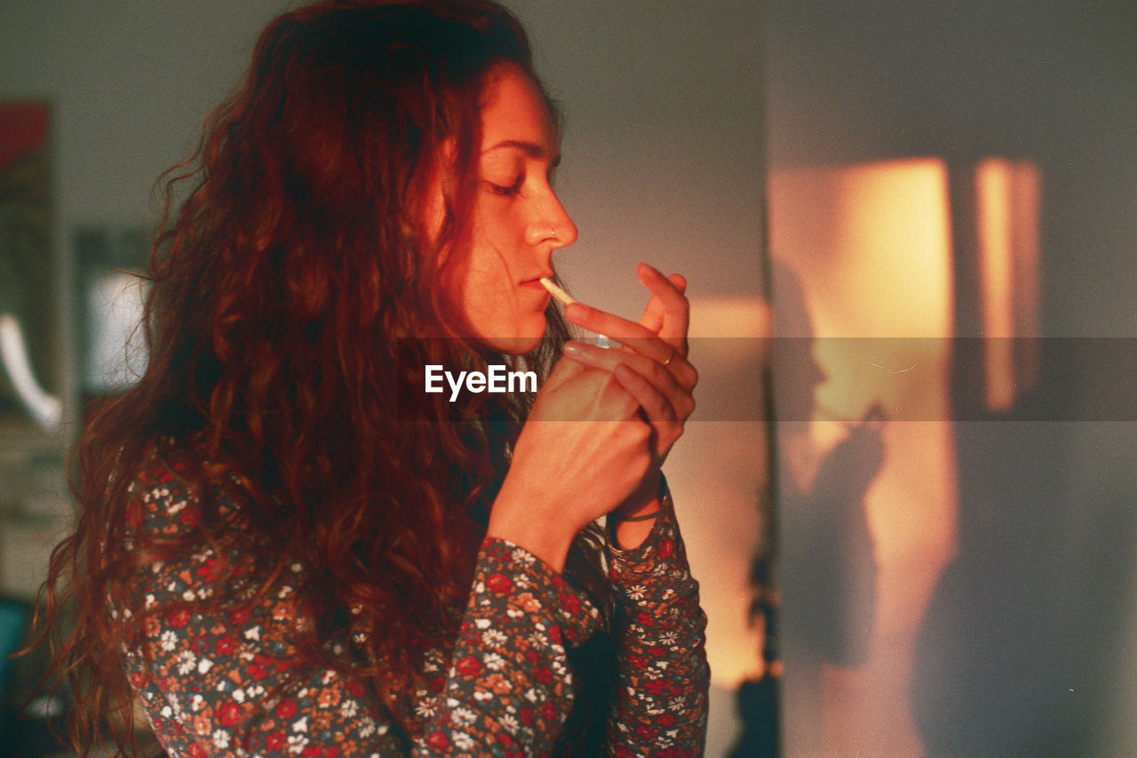 Young woman lighting cigarette at home