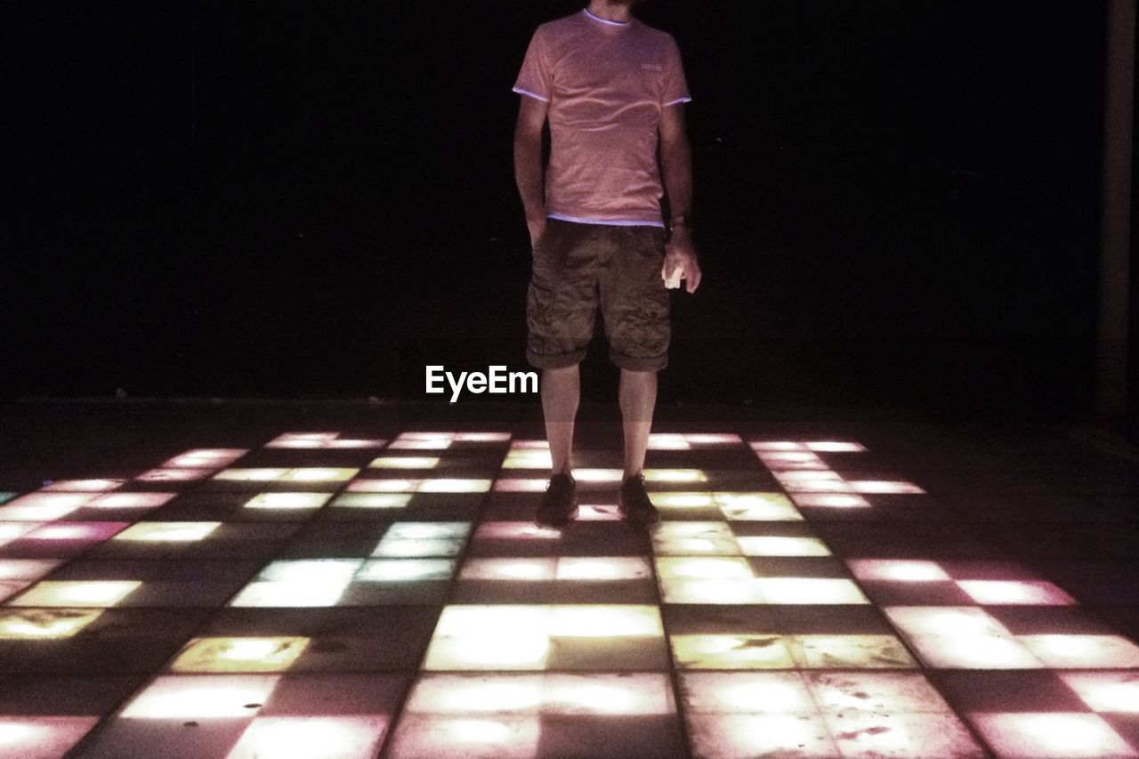 Low section of man standing on illuminated dance floor at night club