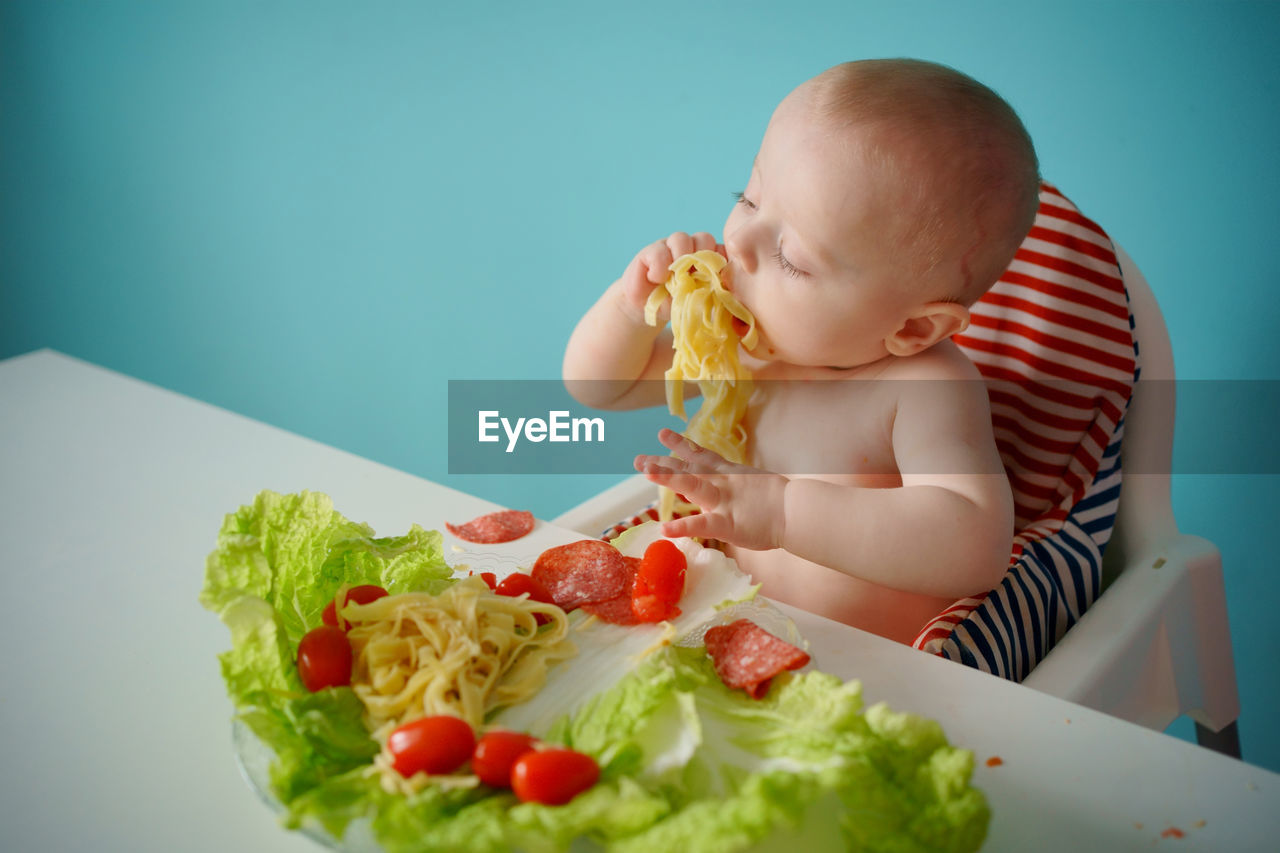 A child eats pasta with lettuce and tomatoes