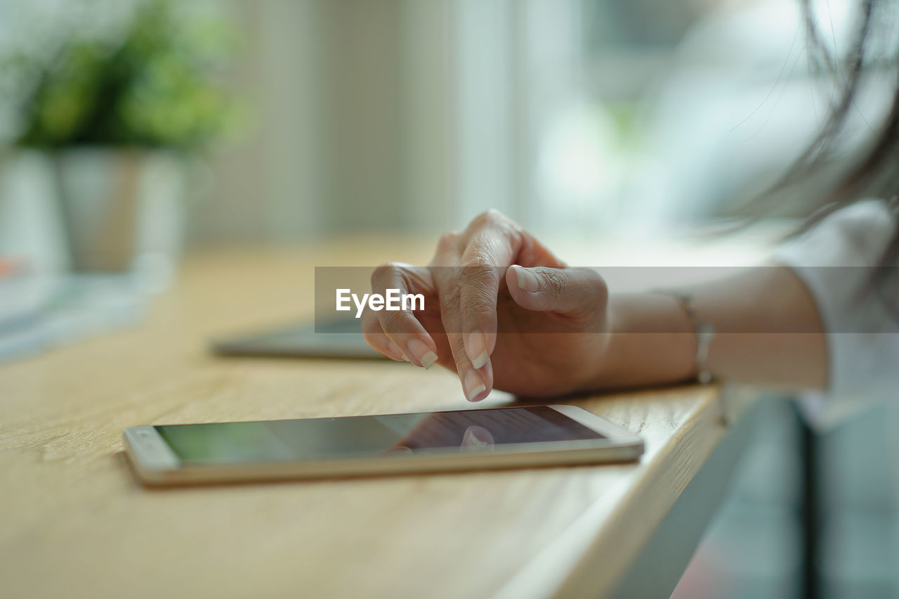 Cropped hand of woman using smart phone on table