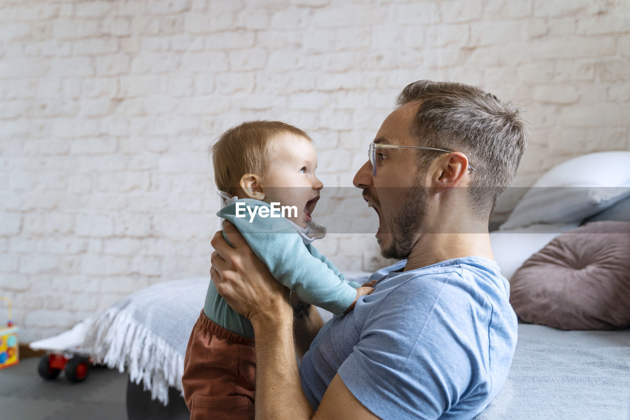 Playful father screaming with baby boy at home