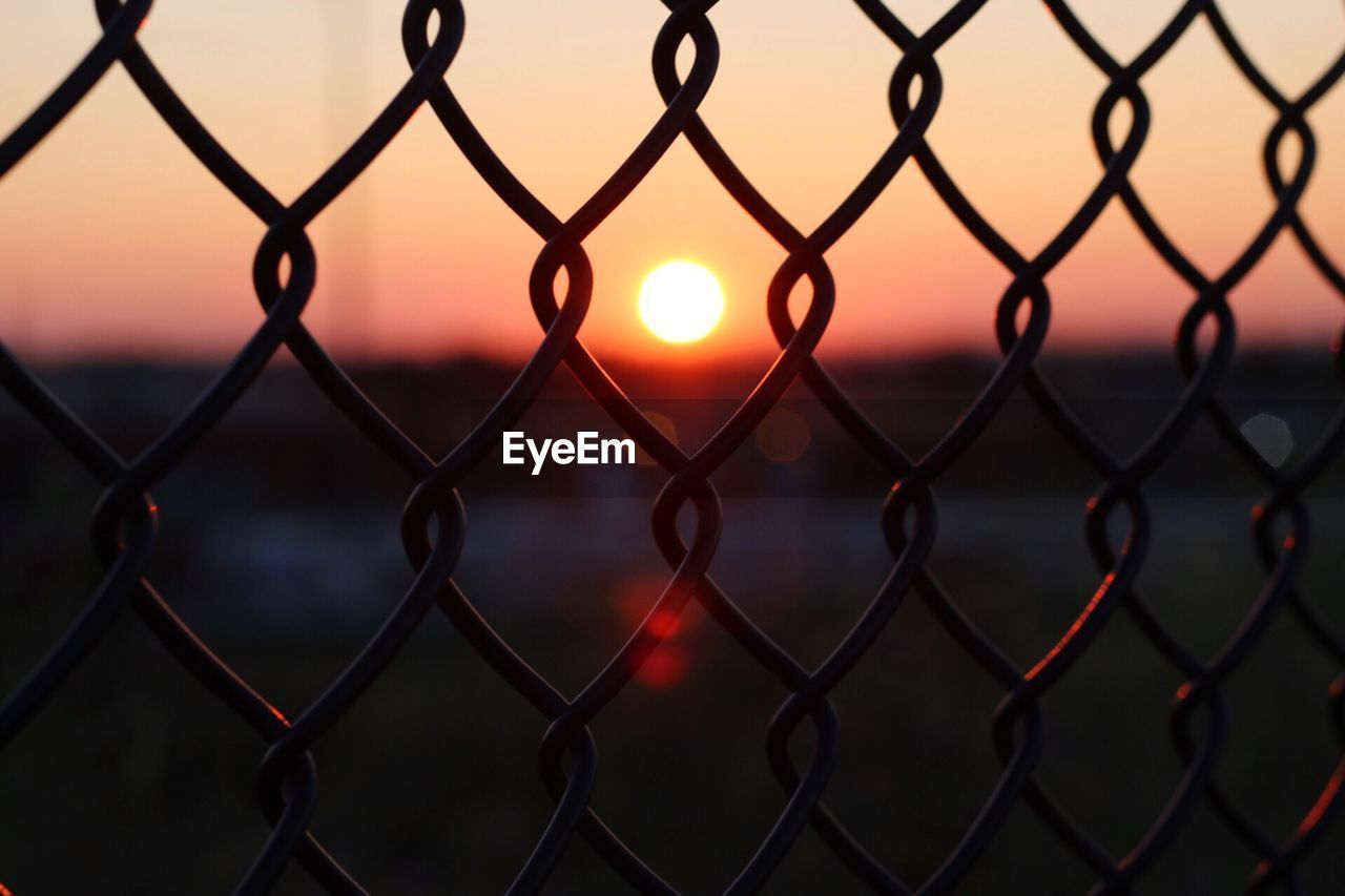 Full frame shot of chainlink fence against sky during sunrise