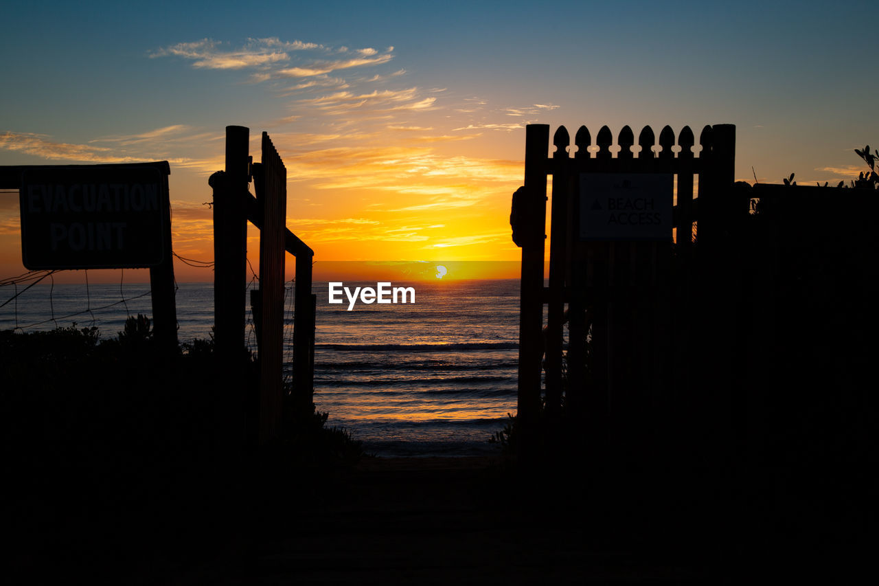 Silhouette wooden posts on beach against sky during sunrise