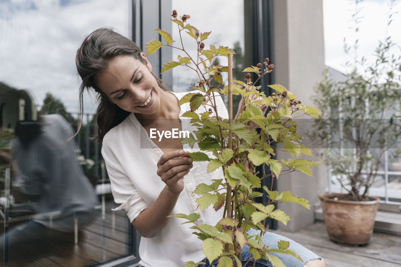 Smiling woman caring for plant on balcony