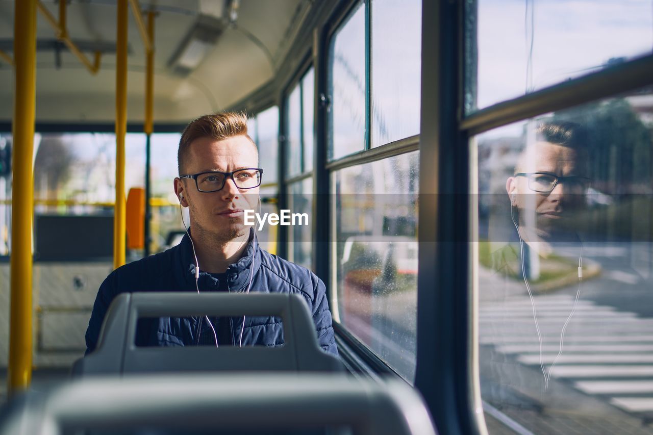 Man listening music on headphones while sitting by window in bus