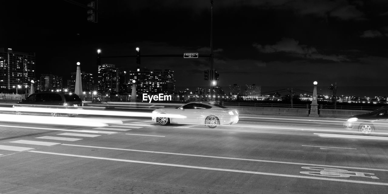 CARS ON ROAD AGAINST ILLUMINATED CITY AT NIGHT