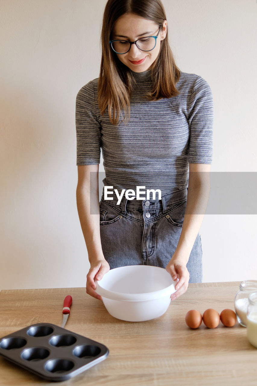 Woman in t-shirt and jeans preparing homemade cupcakes in her kitchen