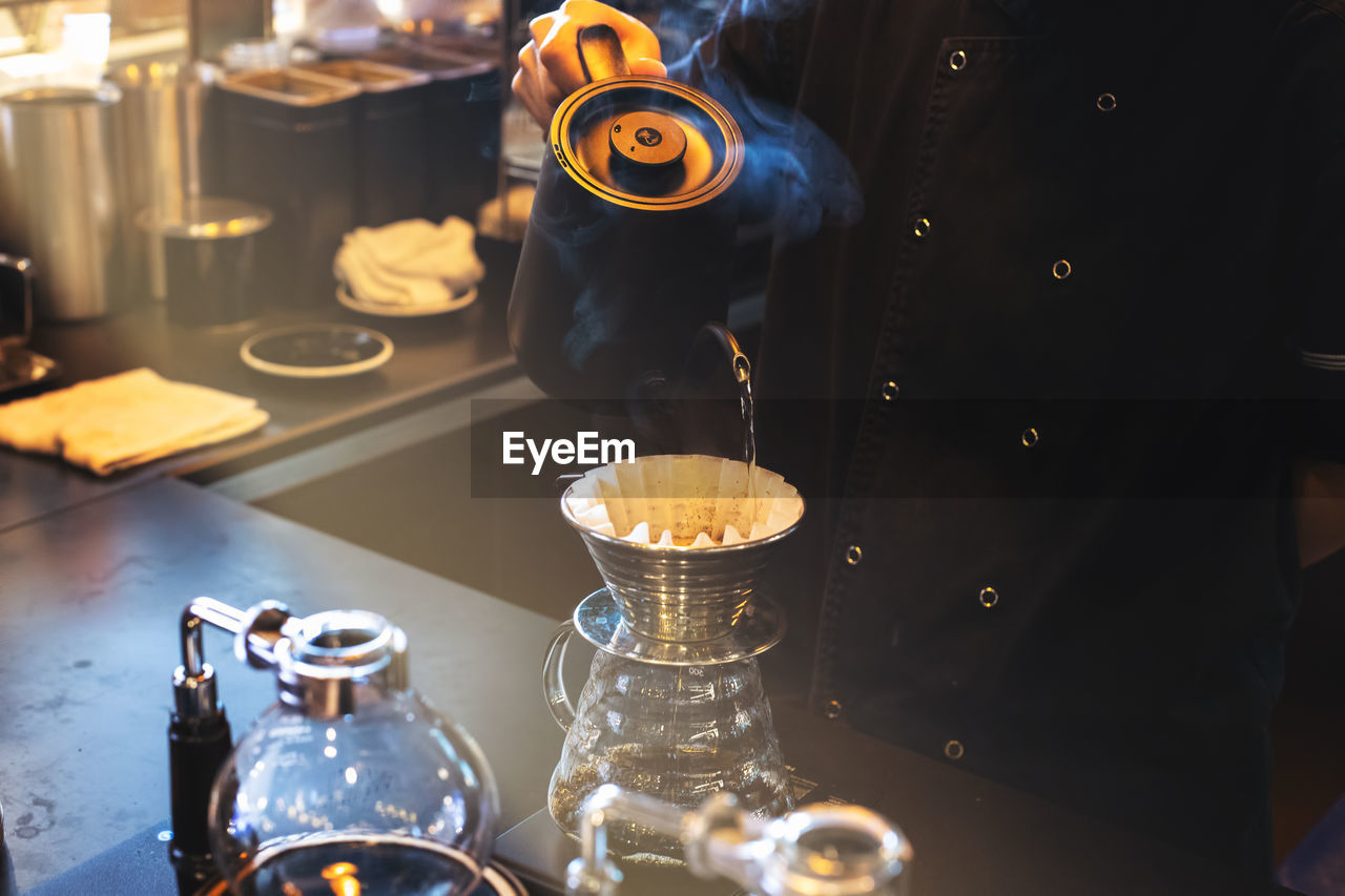 Hand drip coffee, barista pouring hot water on roasted coffee ground with filter in coffee shop.