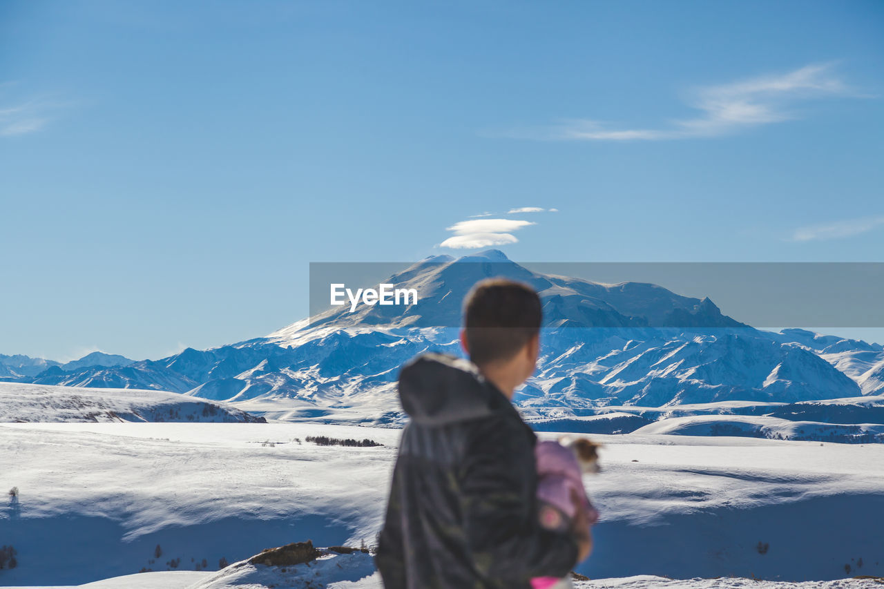 Rear view of man standing on snowcapped mountains against sky