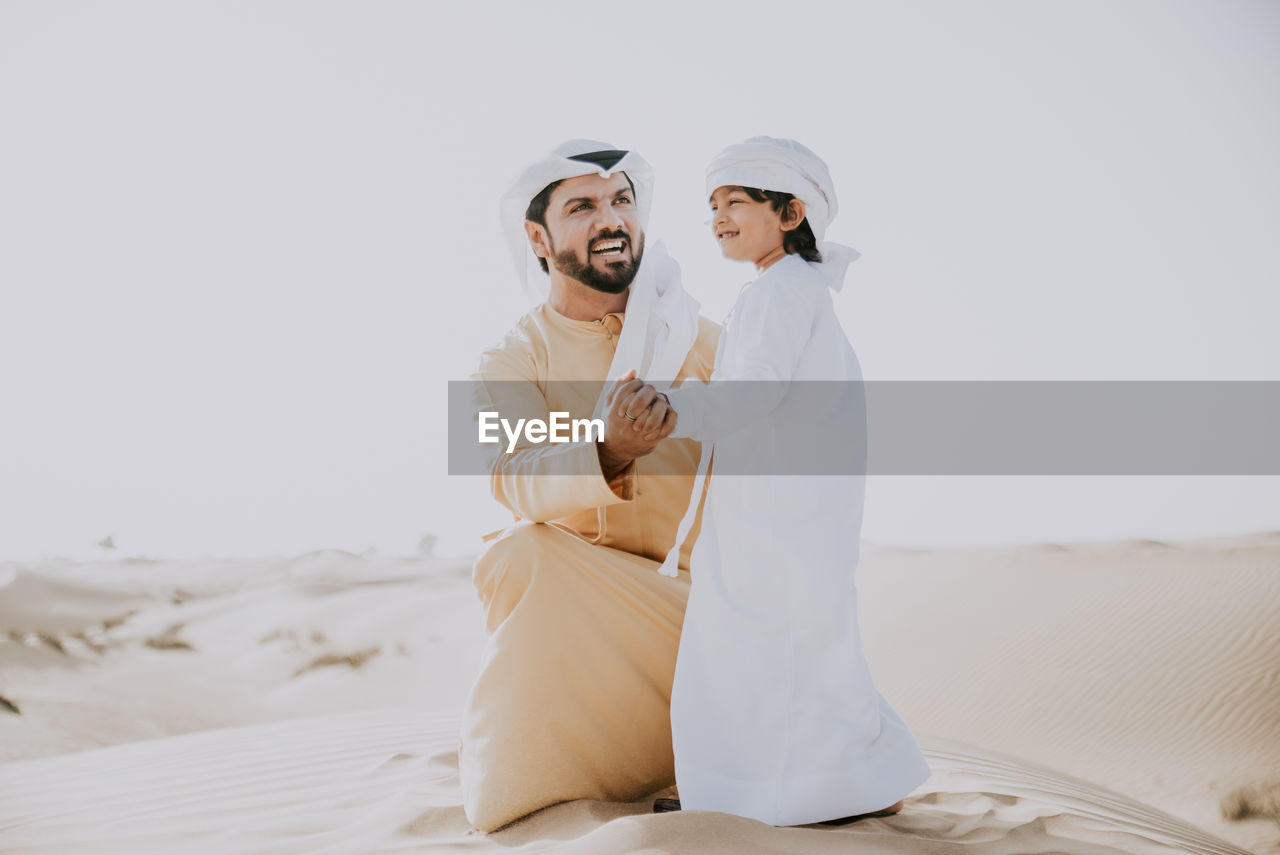 Father and son enjoying while crouching in desert