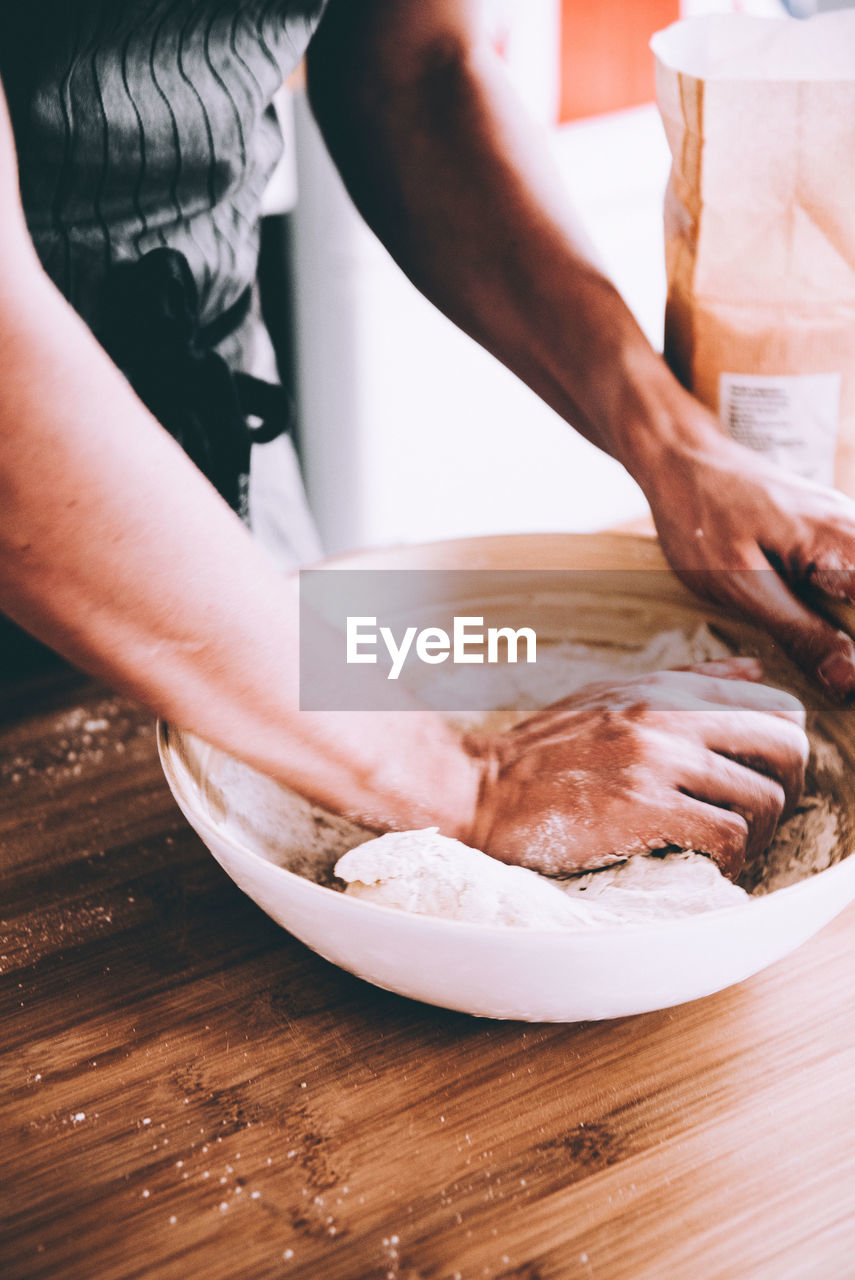 Midsection of man kneading dough in bowl at table