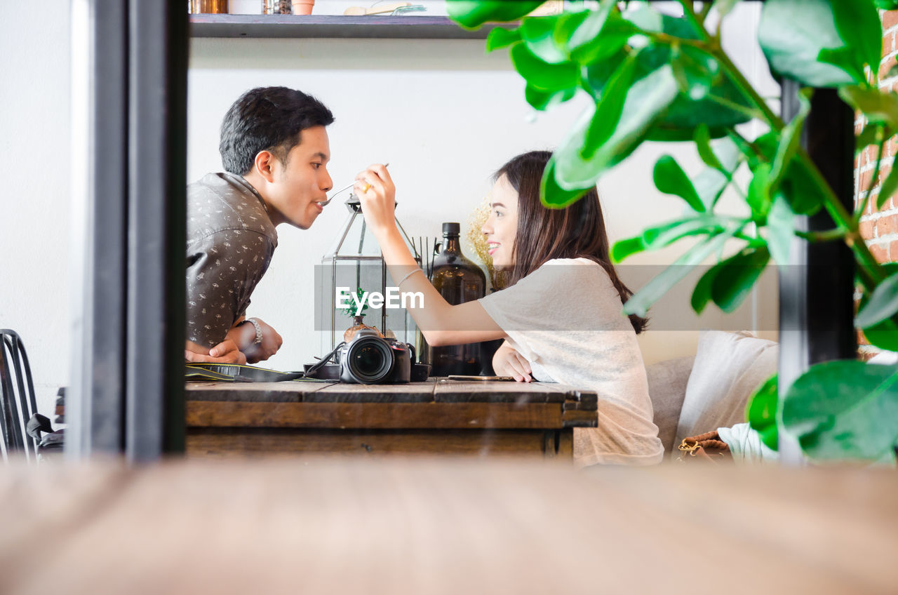 Side view of woman feeding man on table at home