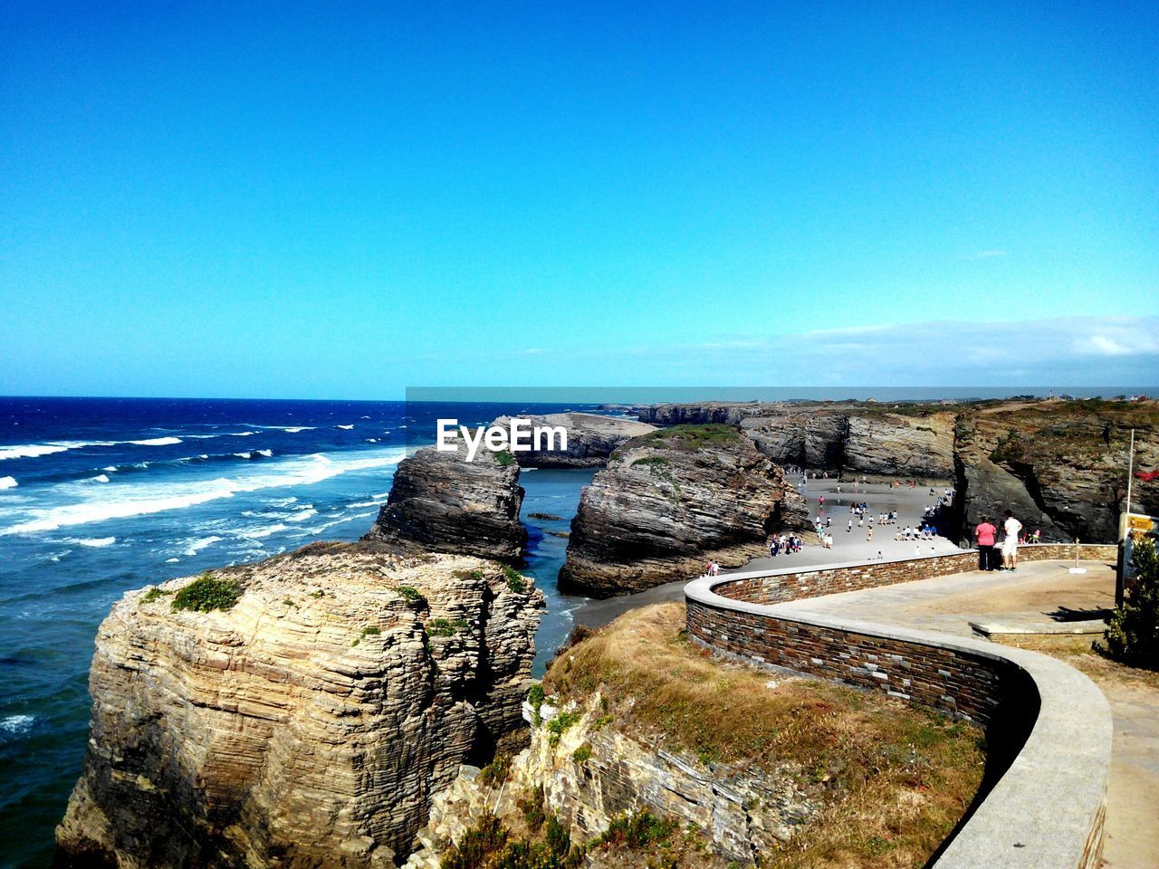 Rear view of man and woman standing at observation point at rocky shore against sky