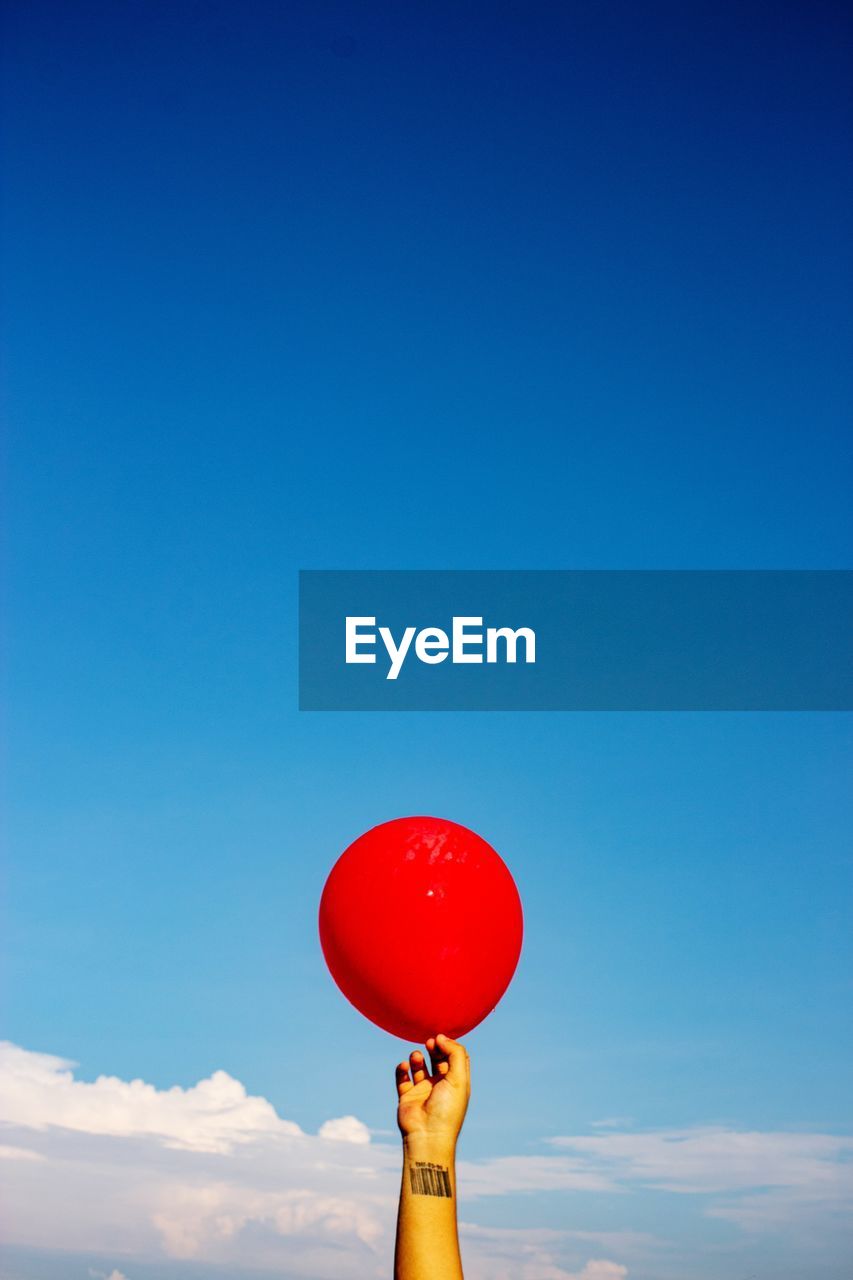 MAN HOLDING BALLOONS AGAINST BLUE SKY