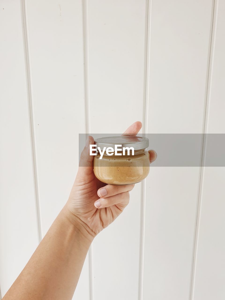 A hand holding a glass of homemade peanut butter