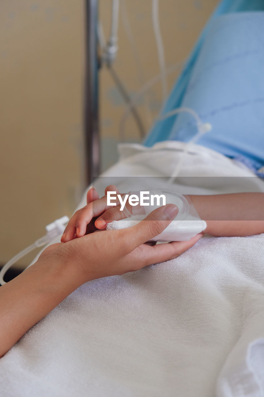 Cropped image of woman holding daughter hand on bed in hospital