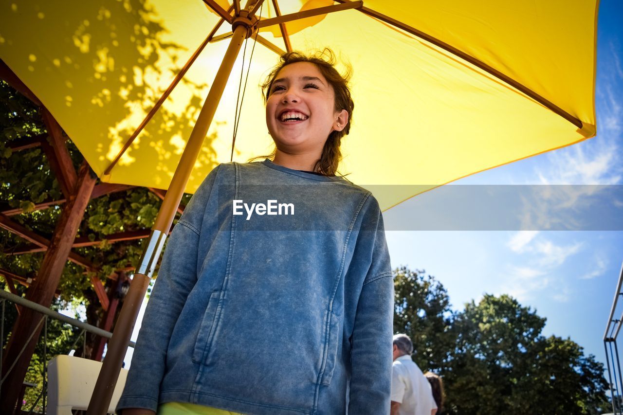 Low angle view of smiling girl standing below parasol