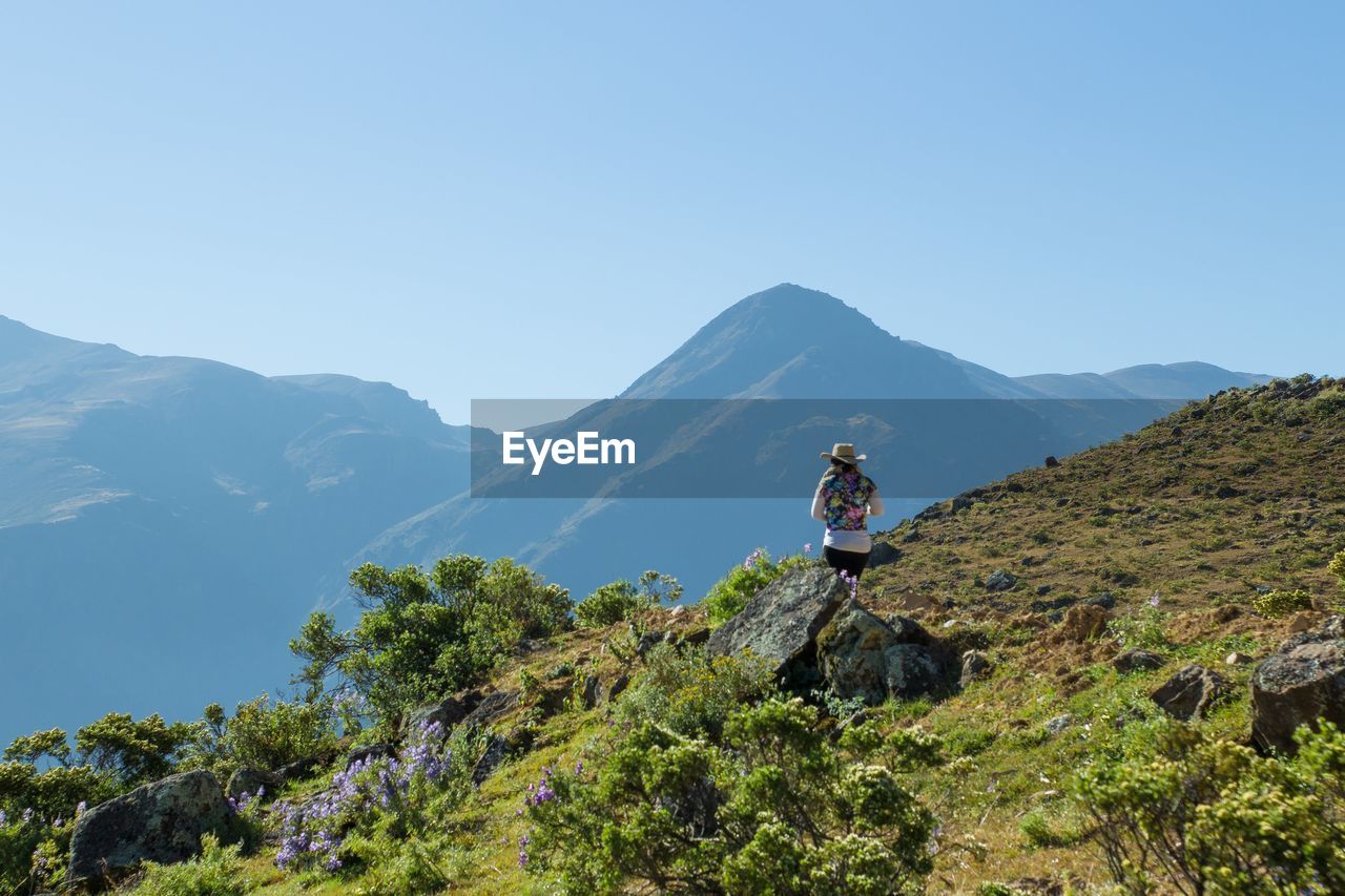 Rear view of woman standing on mountain against clear blue sky