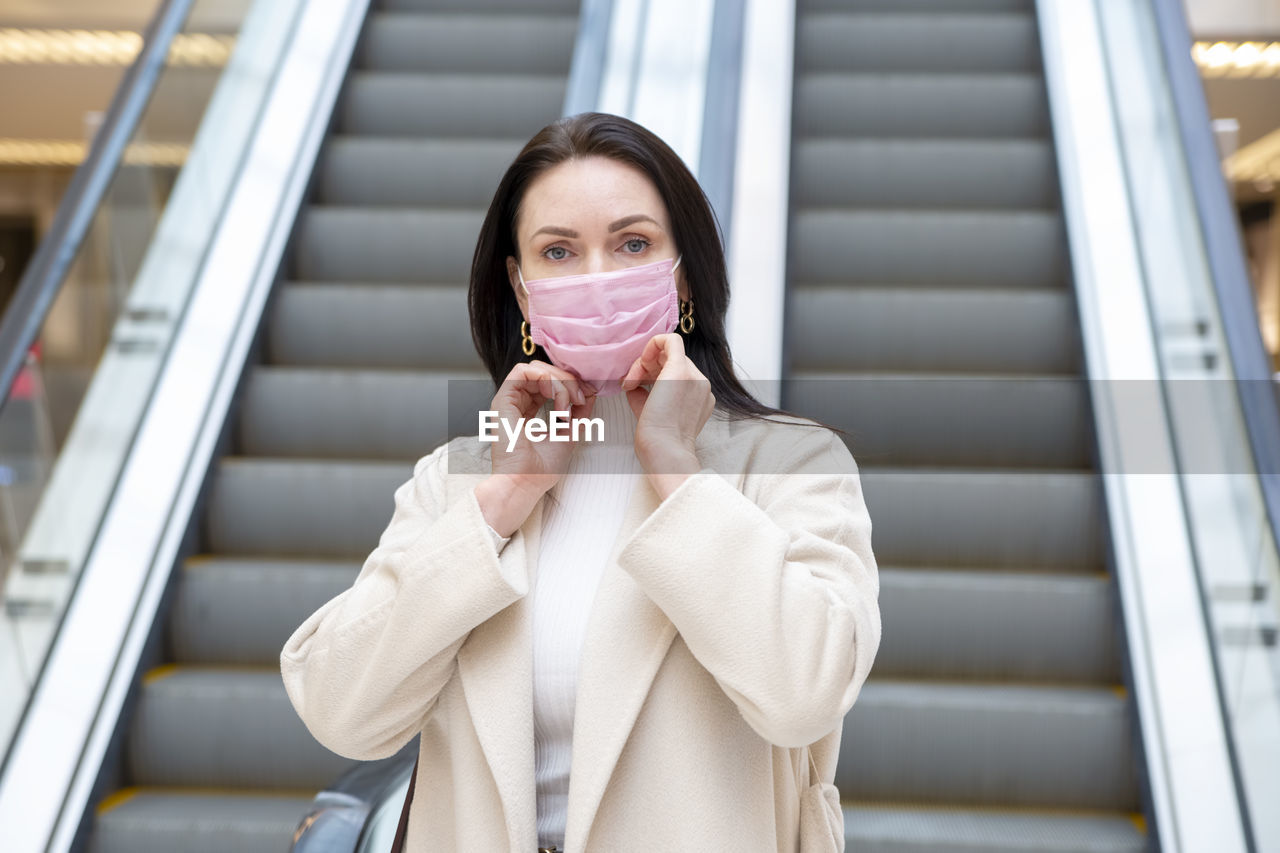 Portrait of woman wearing mask standing against escalator