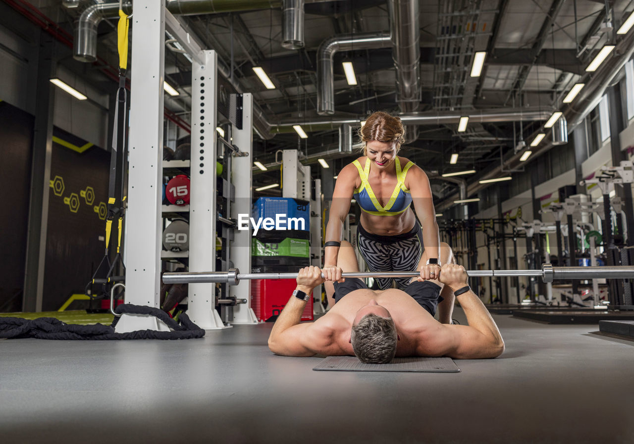 Female instructor assisting man in exercising at gym