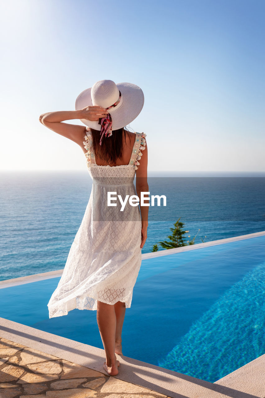 Woman standing by swimming pool against sea