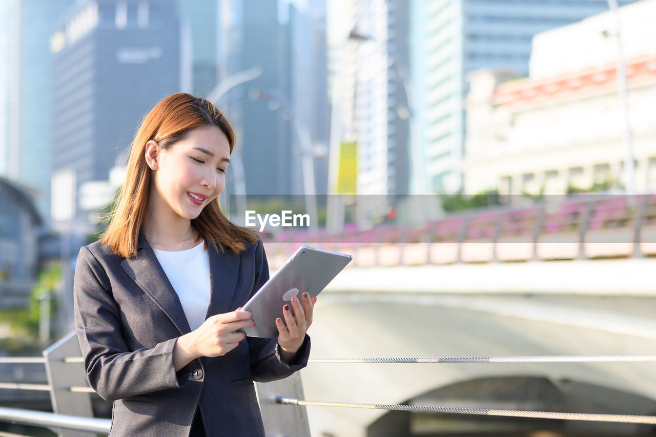 Smiling businesswoman using digital tablet while standing in city