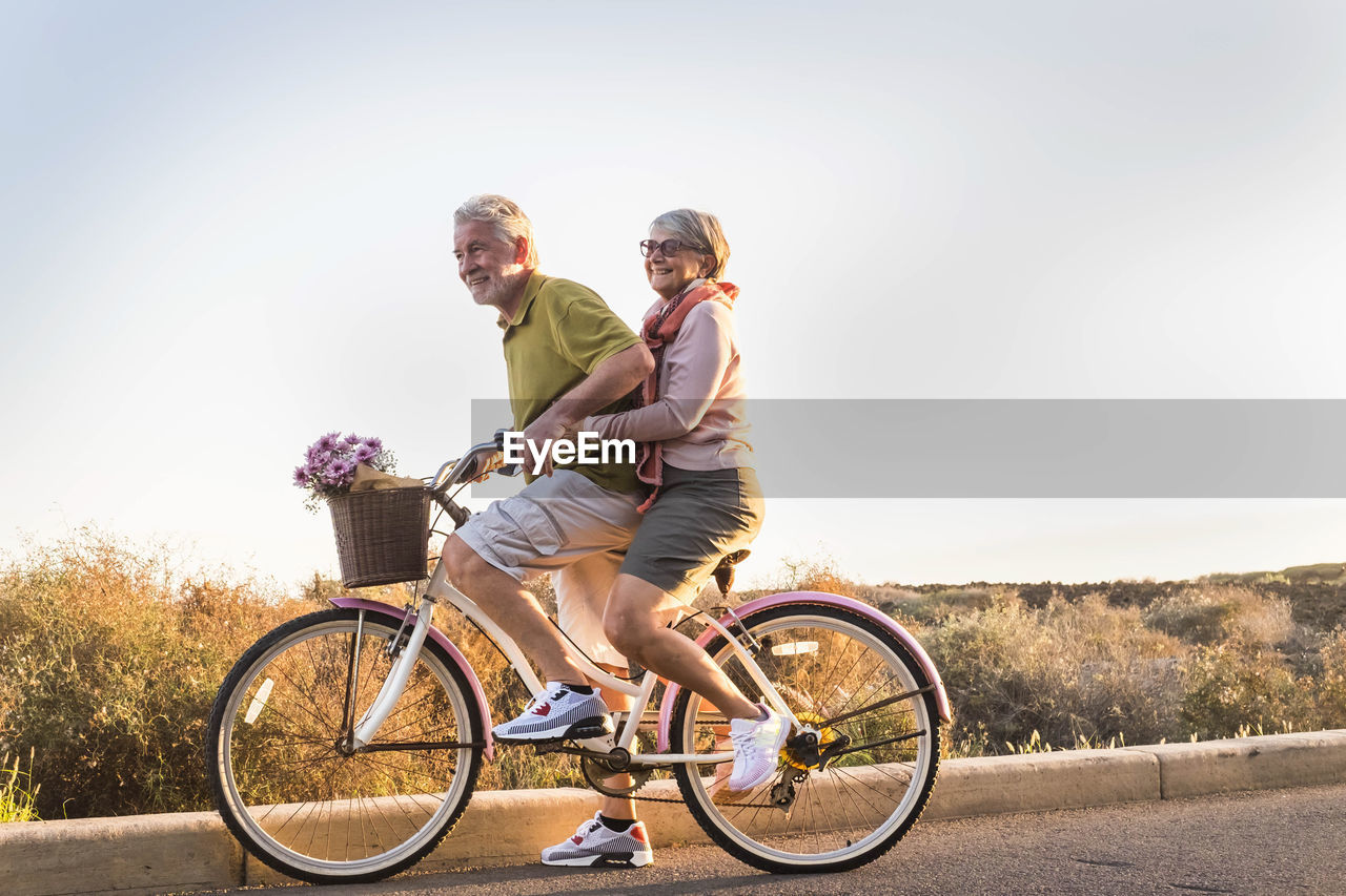 Couple riding bicycle on road against sky