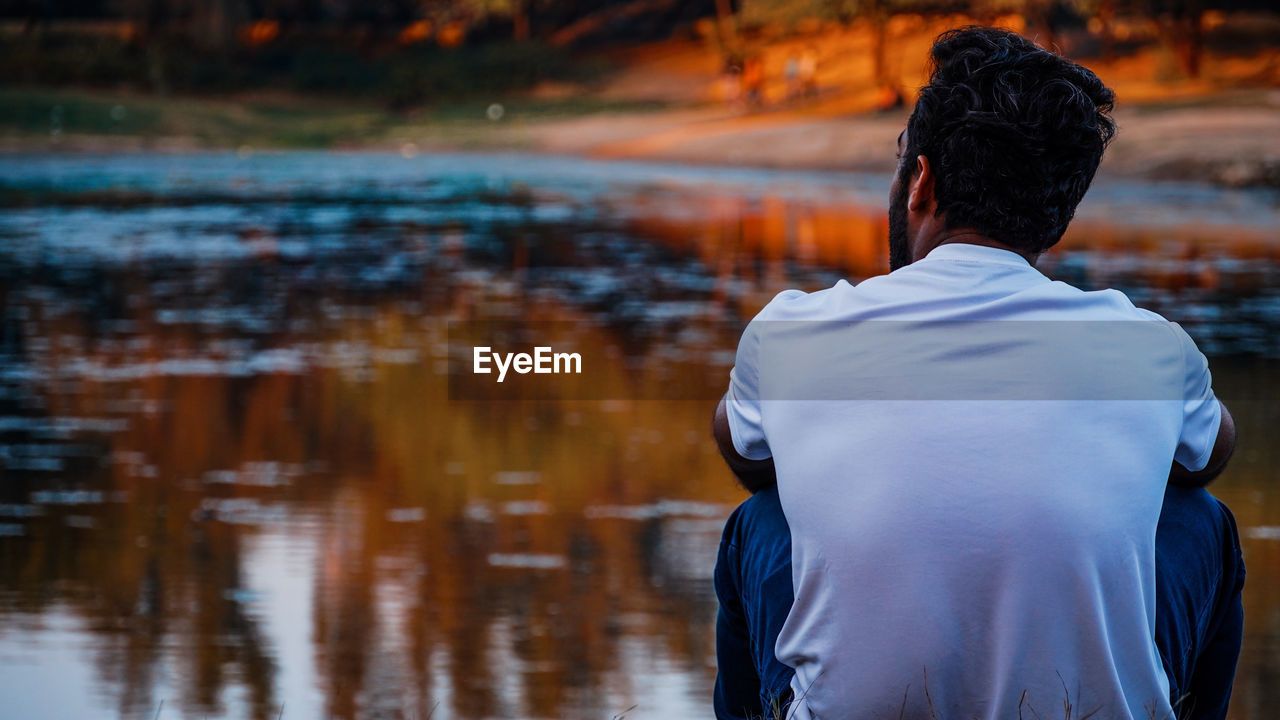 Rear view of young man sitting by lake