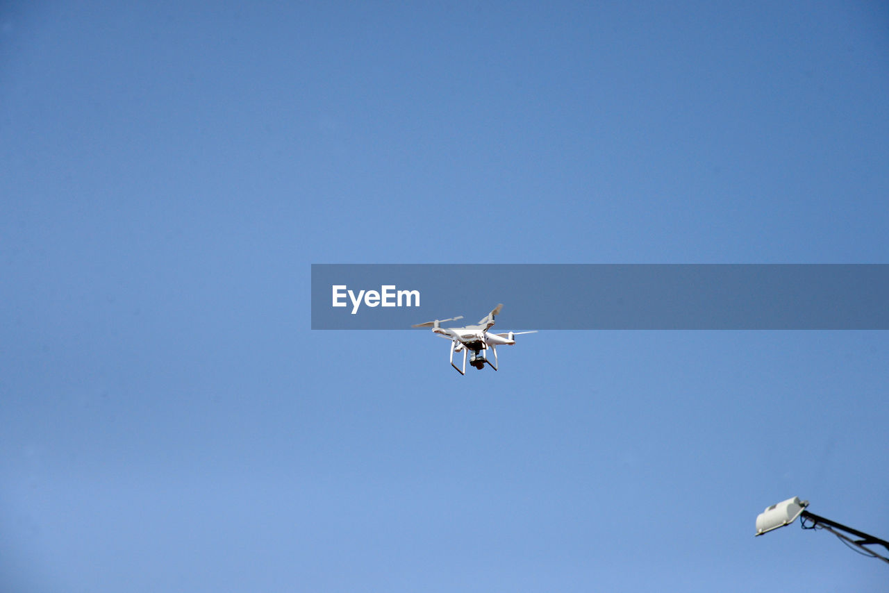 Low angle view of drone flying against clear blue sky