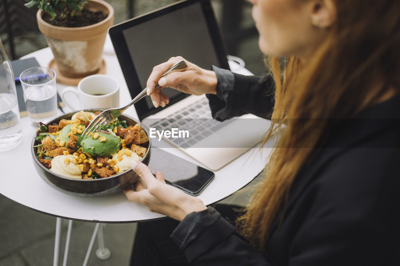 Businesswoman with bowl of meal and laptop at table