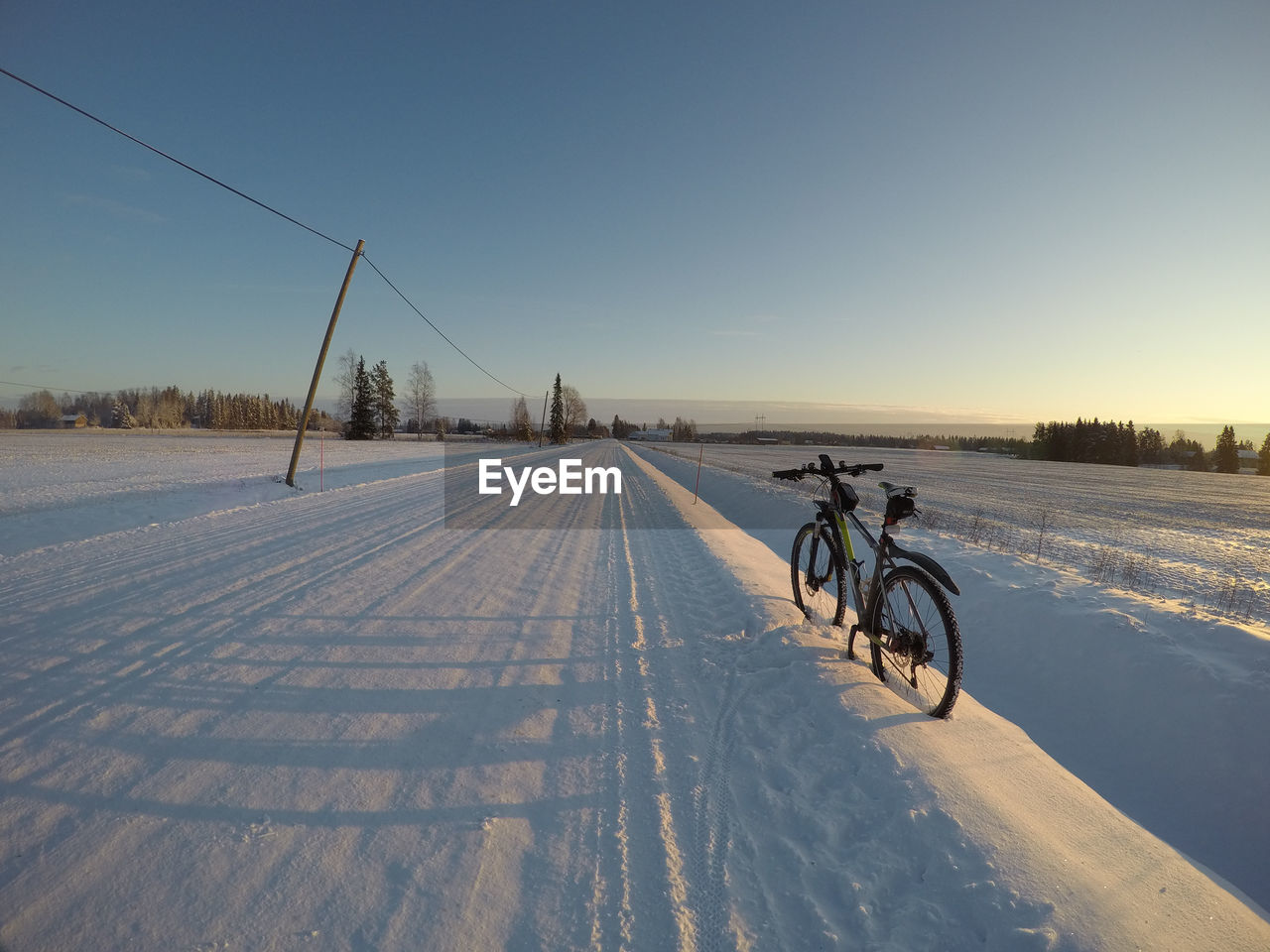 BICYCLE ON SNOW COVERED ROAD AGAINST SKY