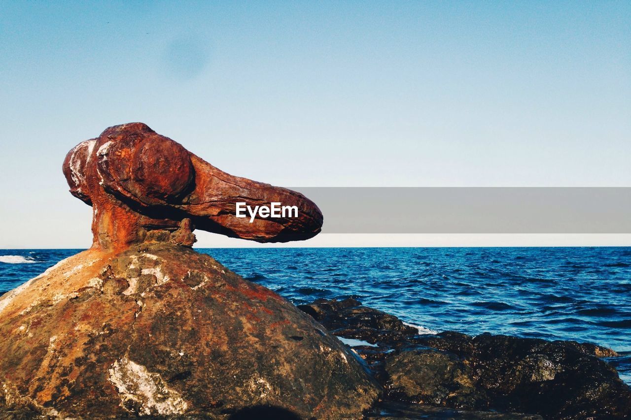 Rock formation and sea against clear sky