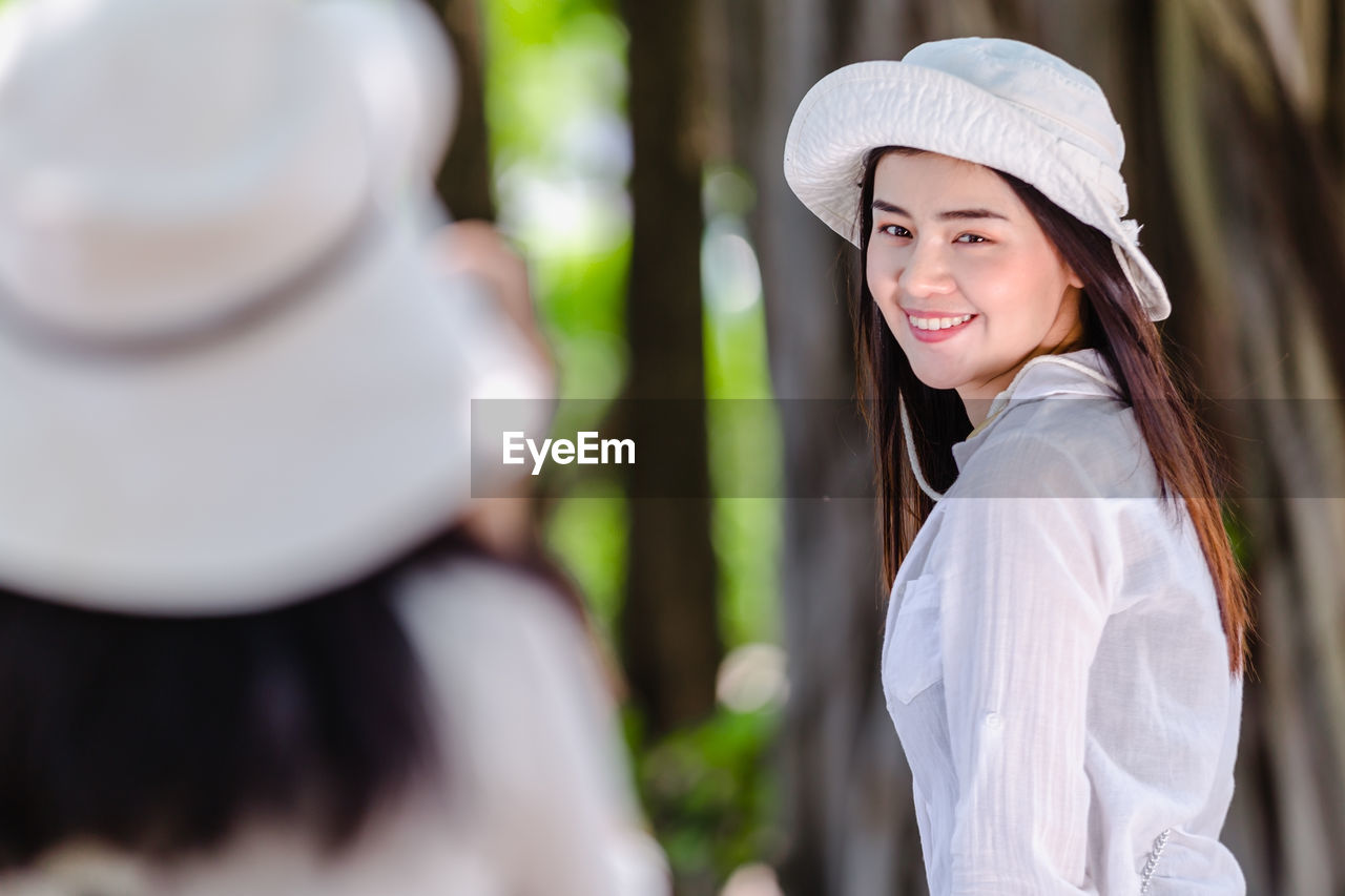 Woman with friend standing against tree trunk in background