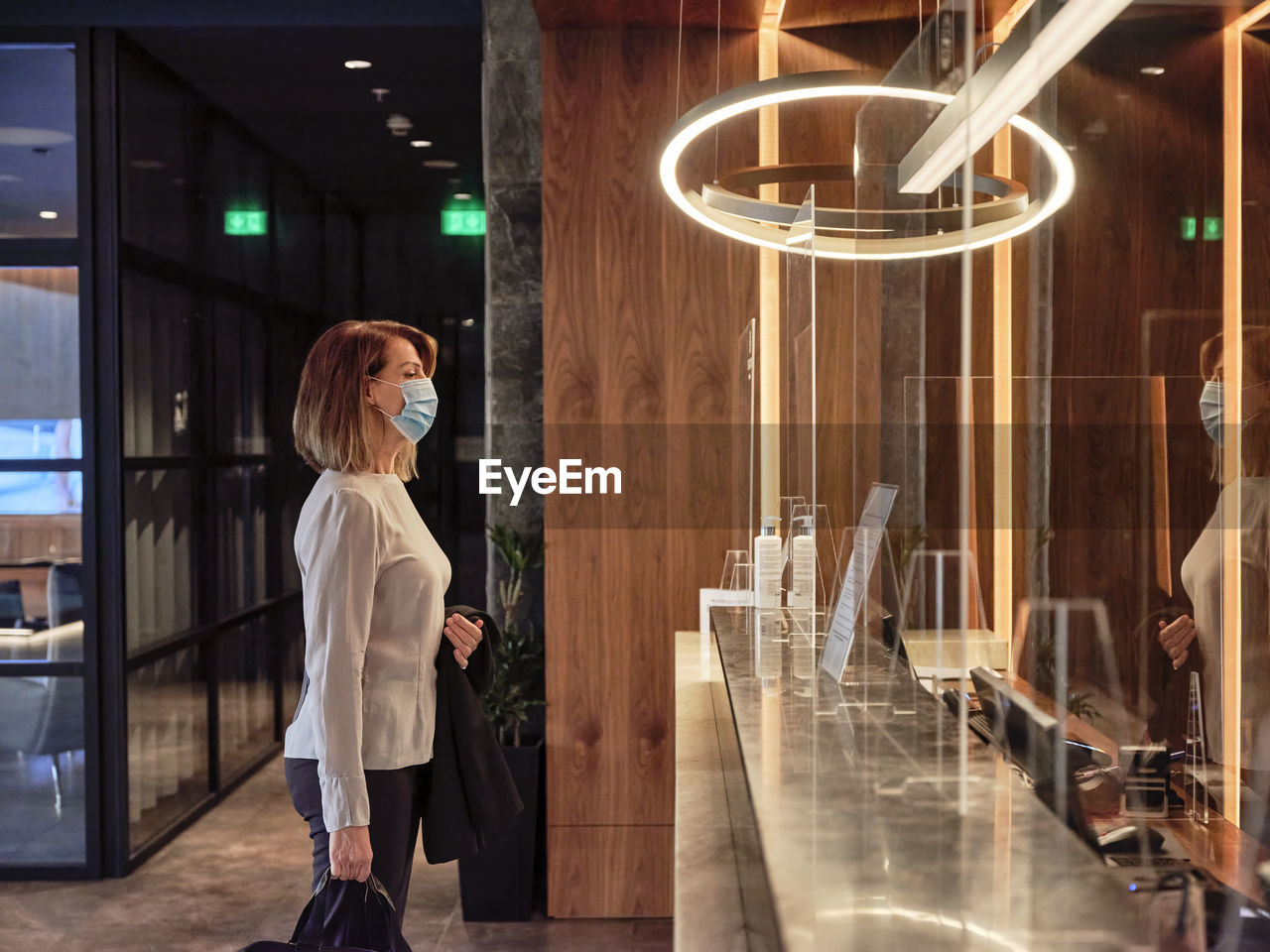 Senior woman looking at glass material while standing in hotel lobby