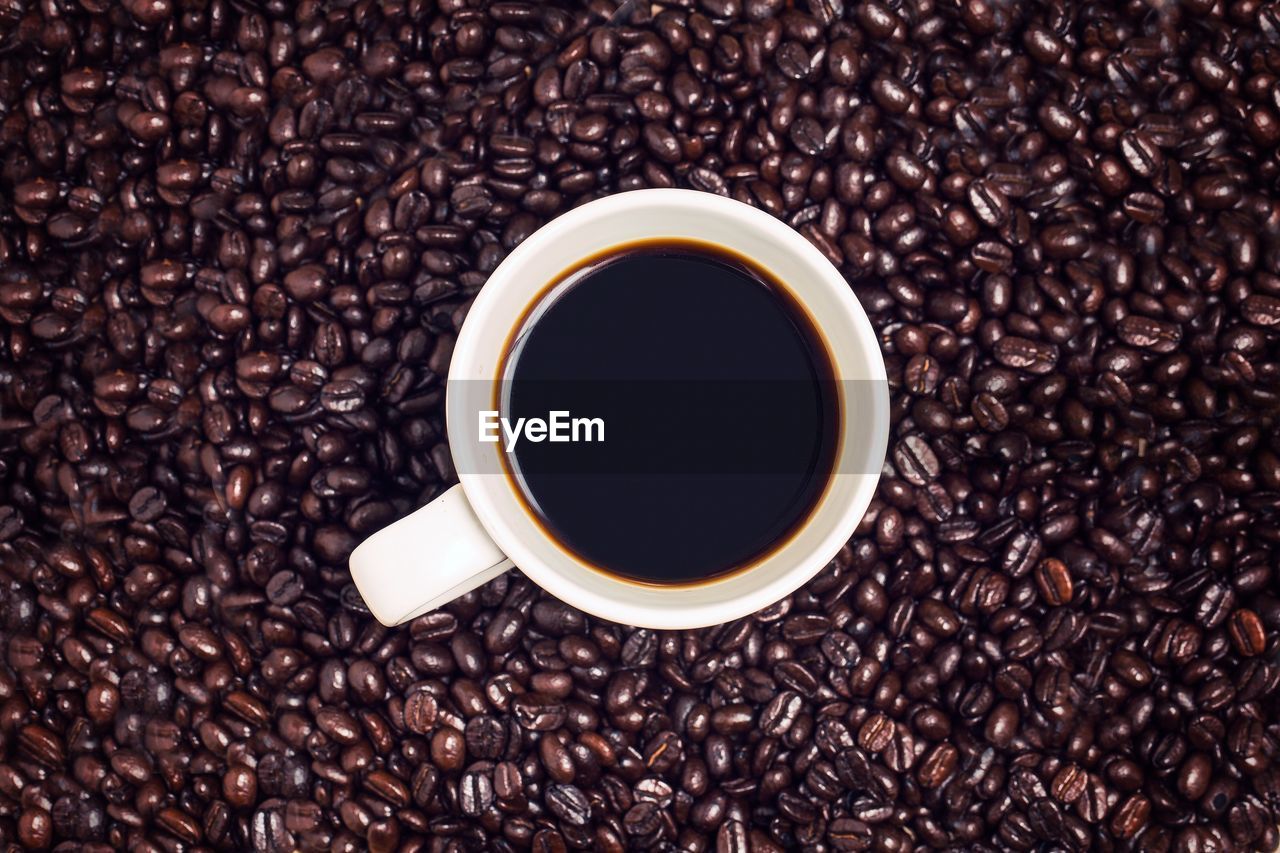 Directly above shot of drink in cup amidst roasted coffee beans on table