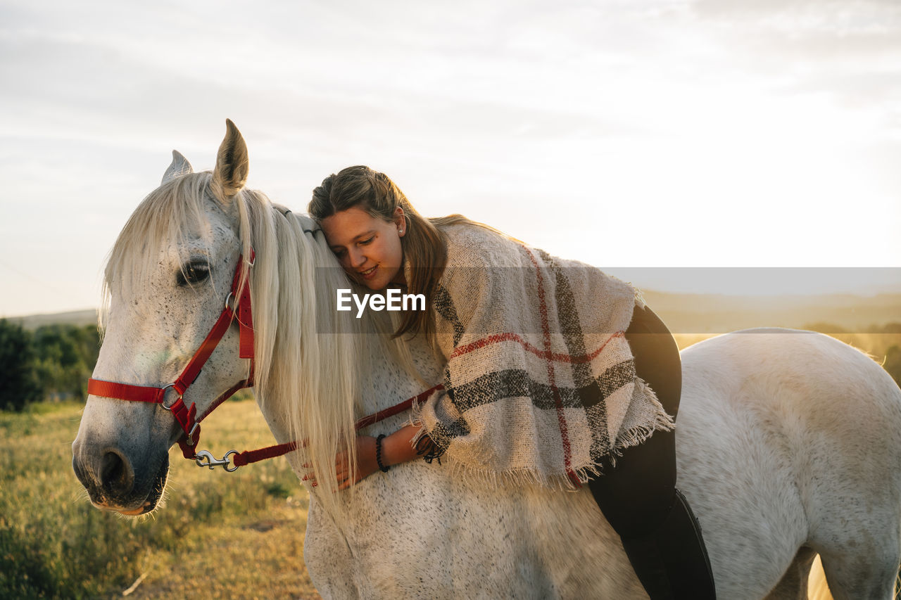 Young woman embracing while riding white horse during sunset