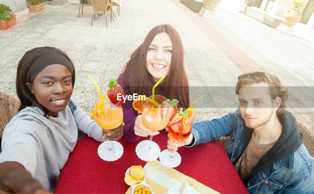 Three friends take a selfie, making cheers, celebrating multicultural friendship.