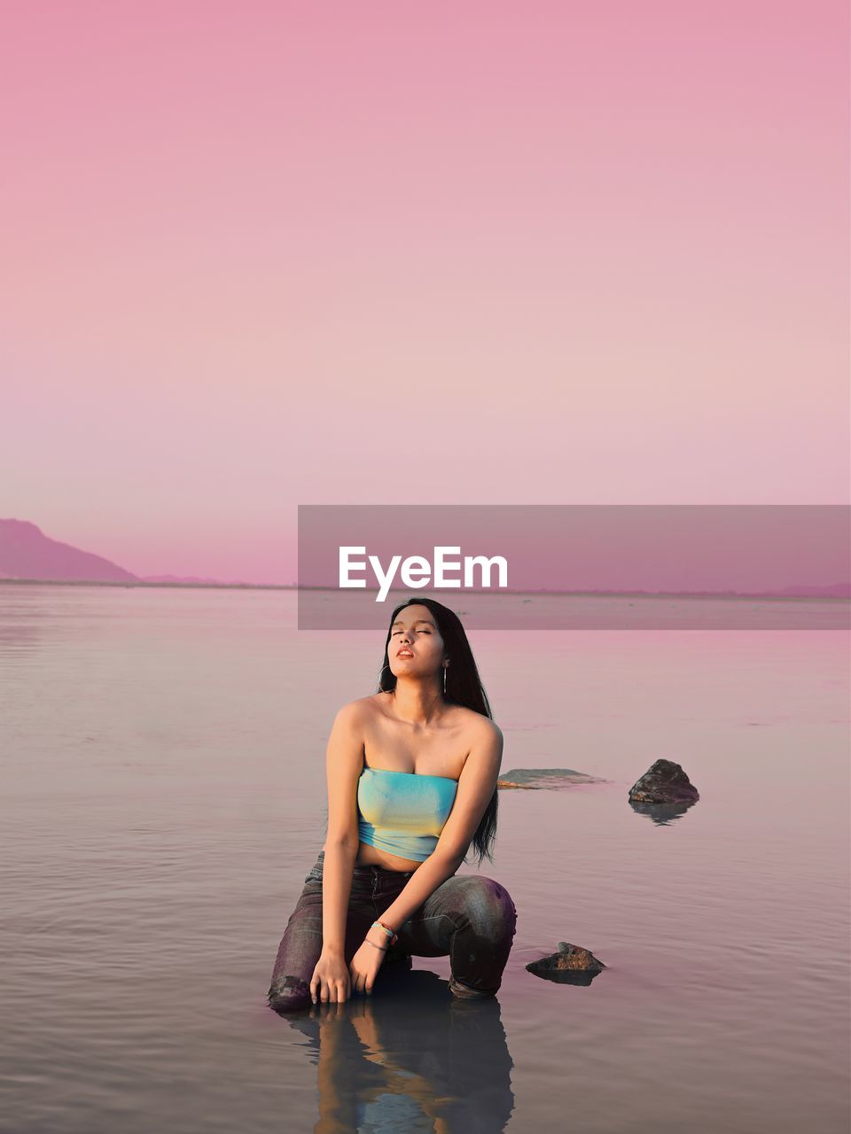 Full length of woman relaxing on beach against sky during sunset