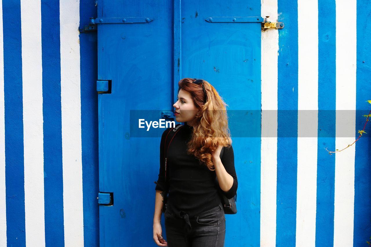 Young woman standing against blue door