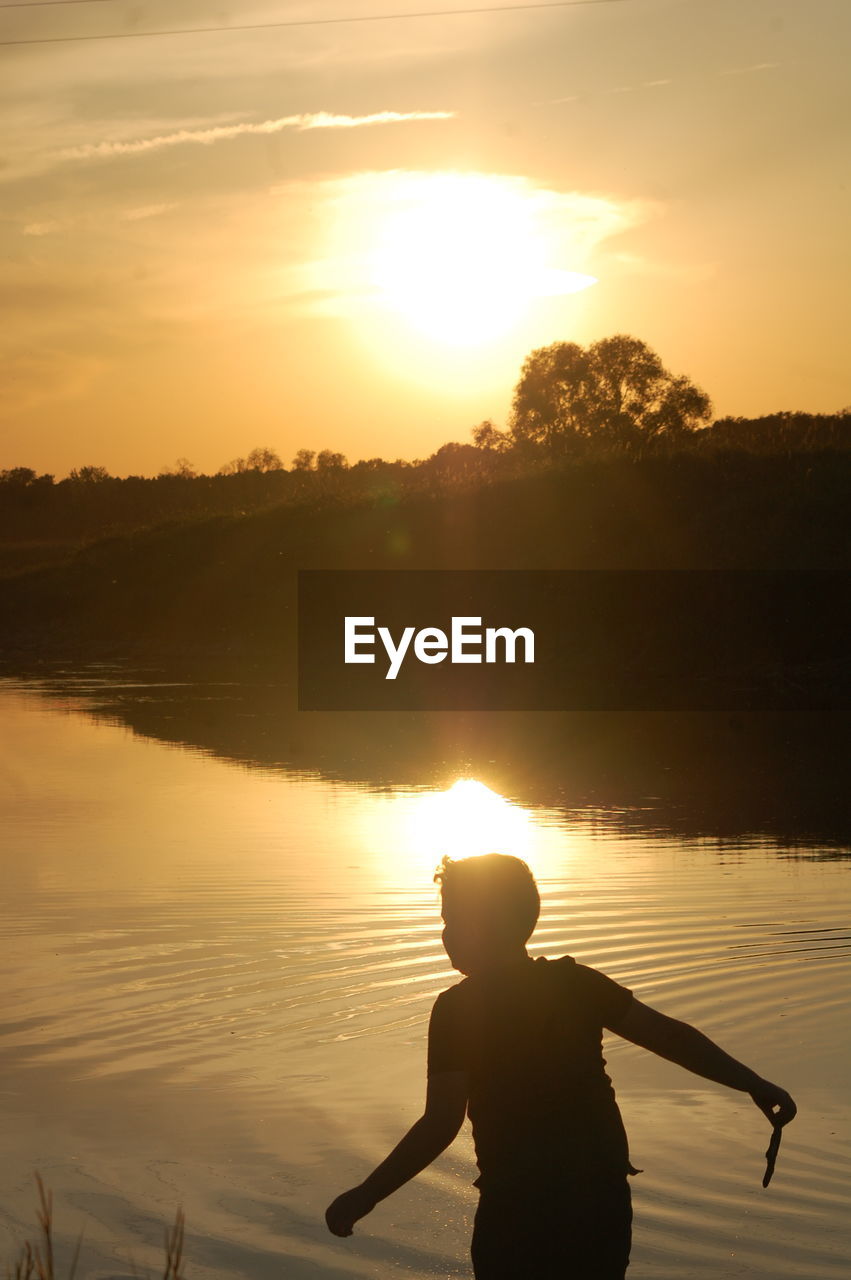 SILHOUETTE MAN ON SHORE AGAINST BRIGHT SUN DURING SUNSET