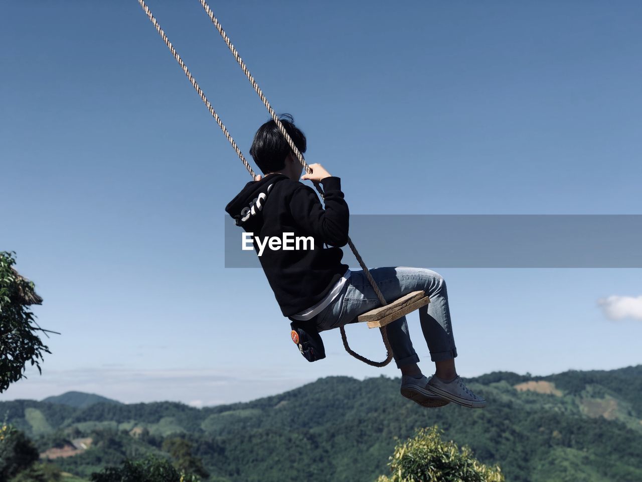 Low angel view of woman sitting on swing against sky