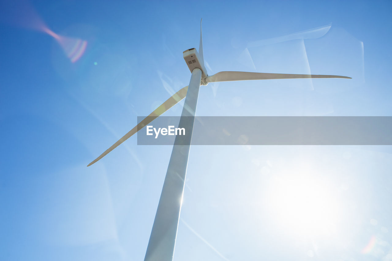 Looking up at wind turbine against blue sky with sun flare