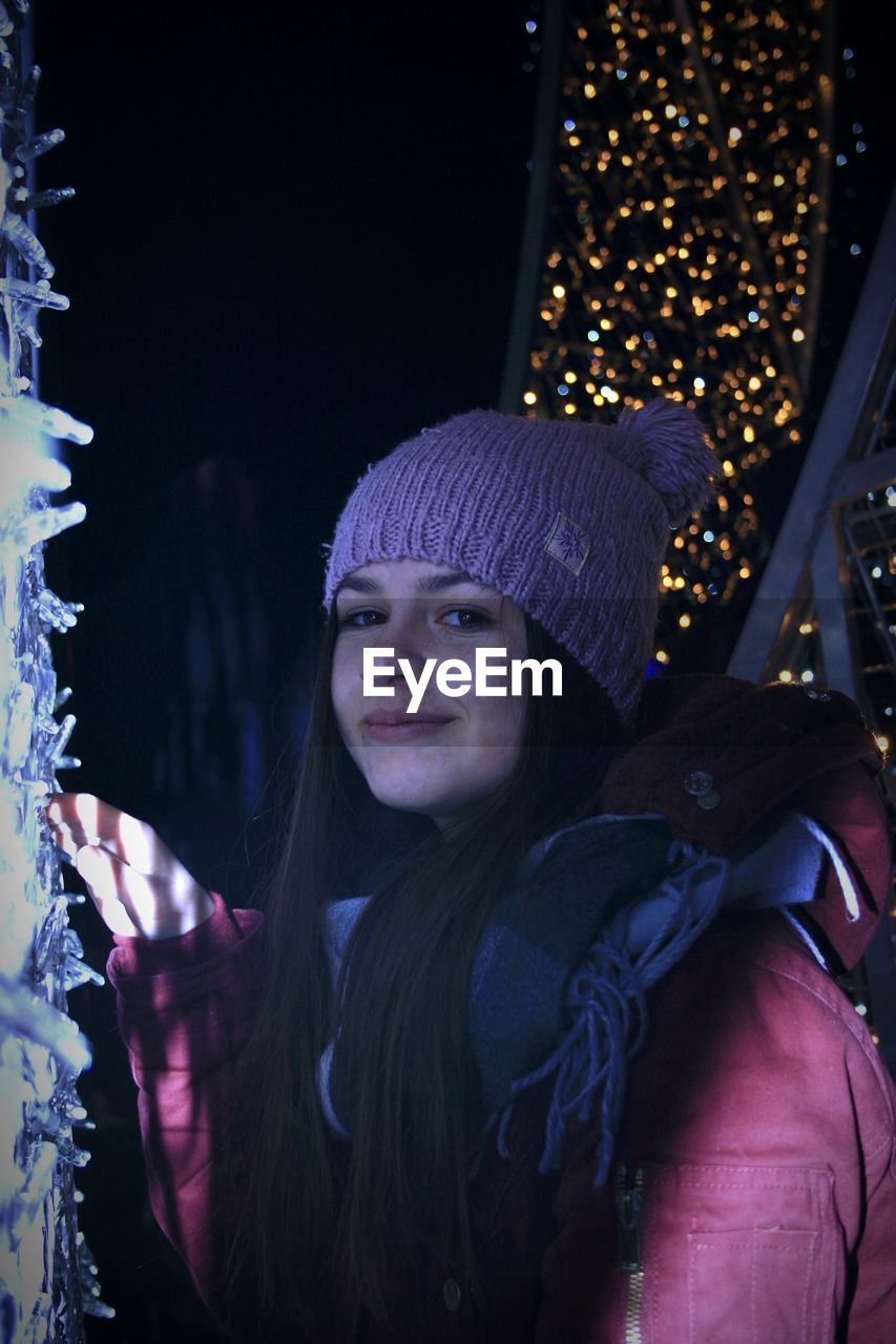 PORTRAIT OF SMILING YOUNG WOMAN IN ILLUMINATED PARK