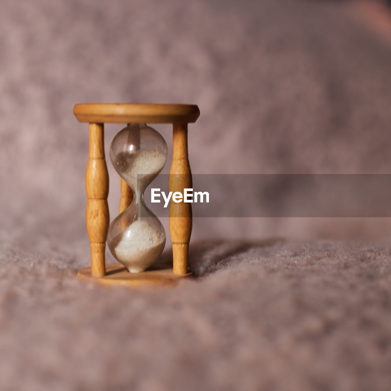 An hourglass on pink background, with the sand flowing down