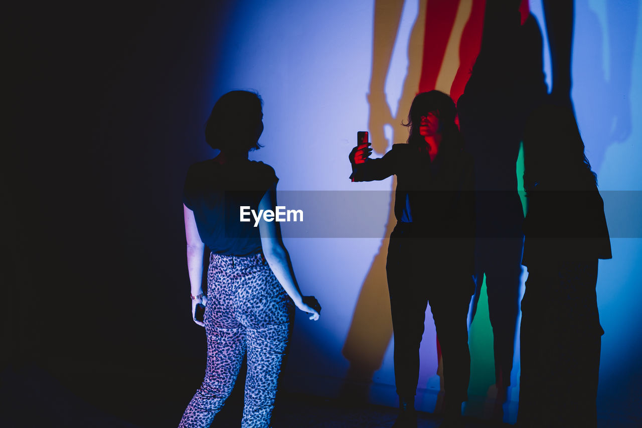 PANORAMIC VIEW OF MAN AND WOMAN STANDING AGAINST ILLUMINATED BLUE WALL