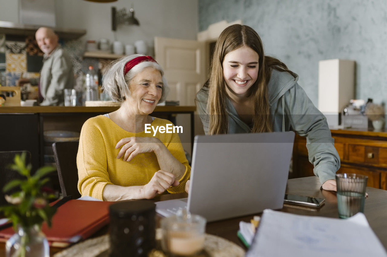 Happy girl teaching grandmother to use laptop at home