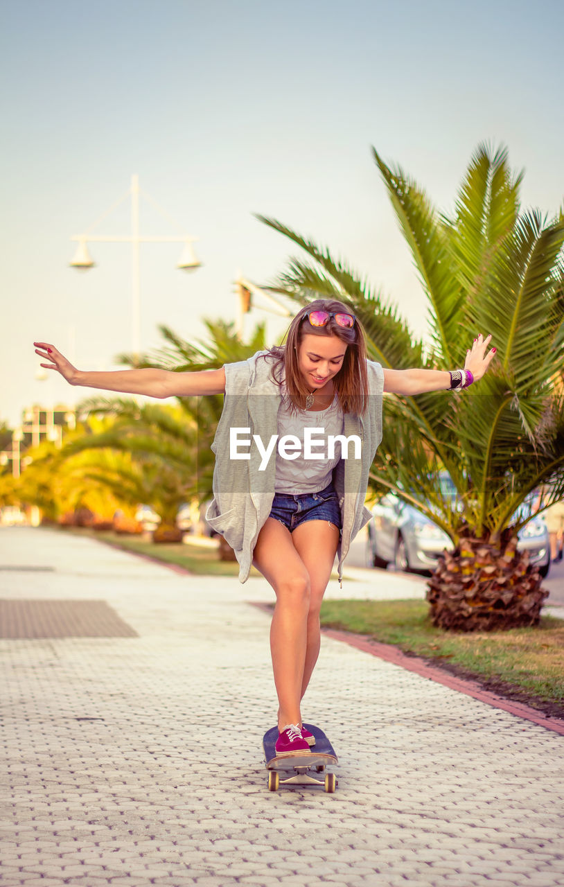 Back view of beautiful young girl with short shorts and skateboard outdoors on a hot summer day