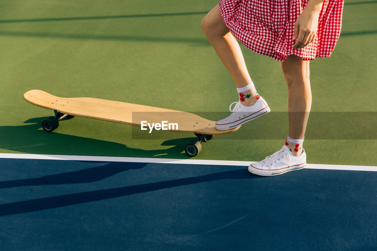 Girl in dress with foot on skateboard on a tennis court