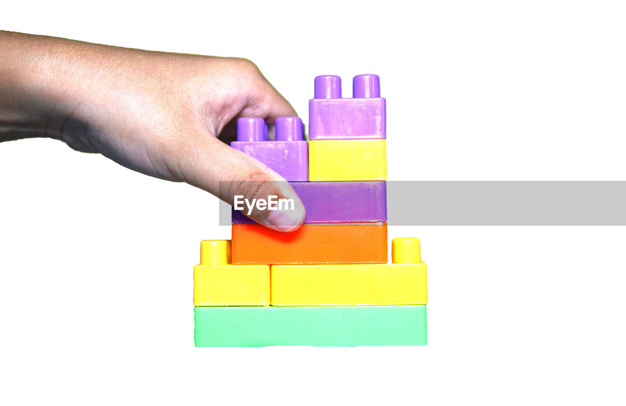 CLOSE-UP OF HAND HOLDING MULTI COLORED TOY AGAINST WHITE BACKGROUND